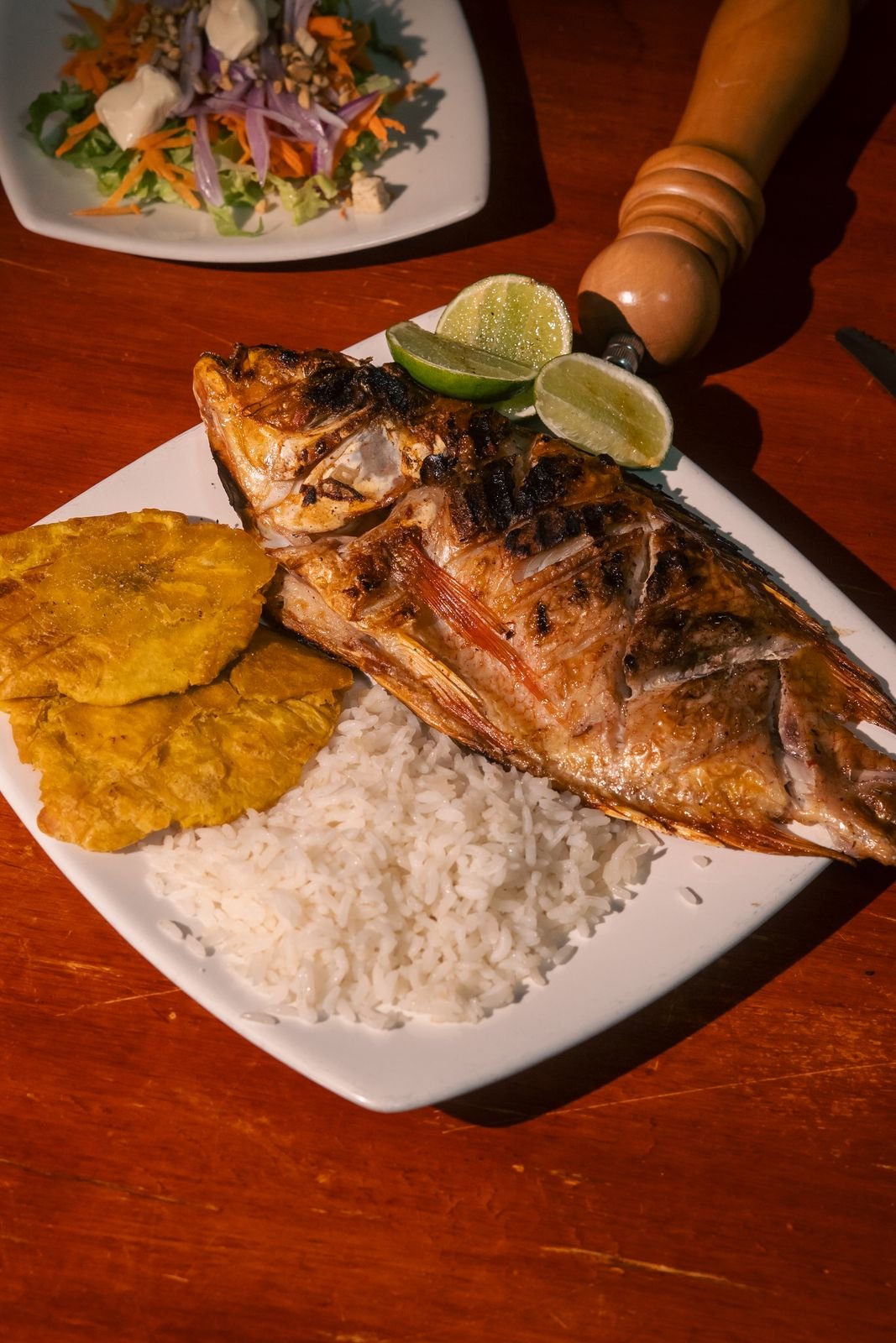 Pescado entero a la parrilla con arroz y patacón sobre mesa de madera