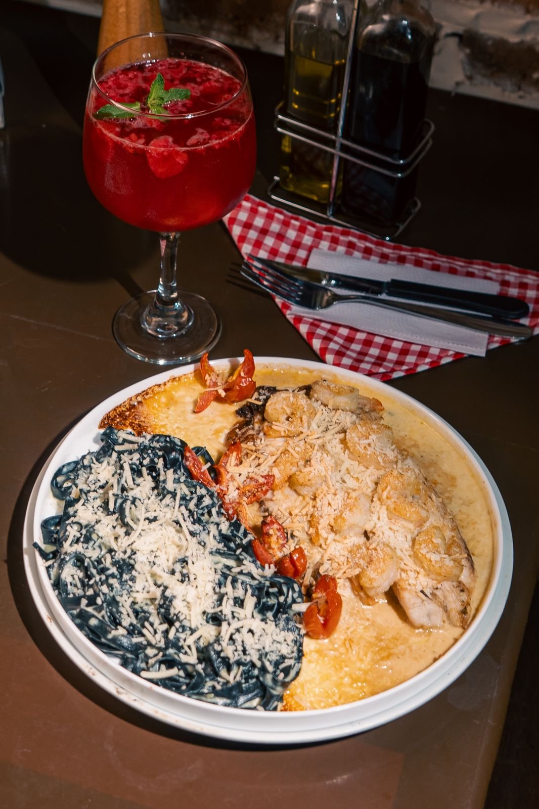 Plato de pasta negra y cremosa con cóctel rojo en restaurante